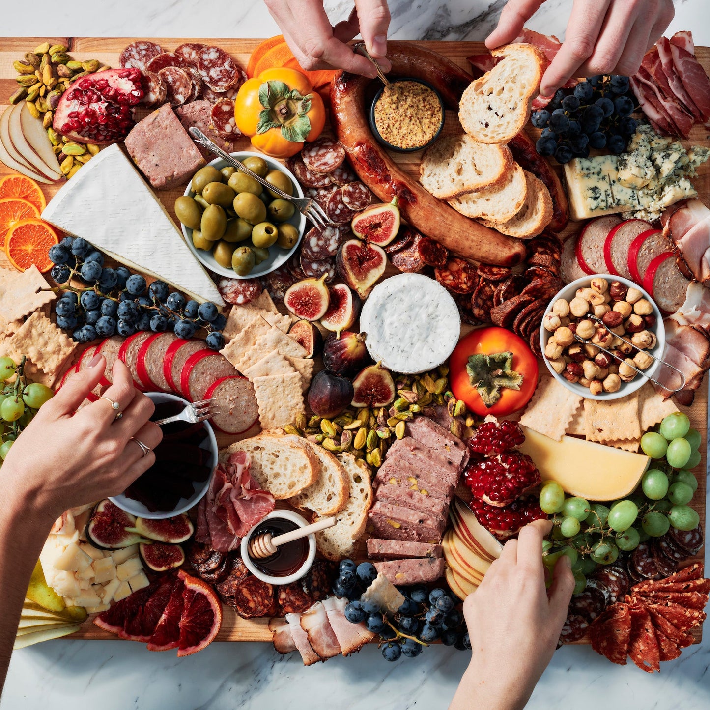 Charcuterie board with various meats, cheeses, fruits, and vegetables on a marble surface.