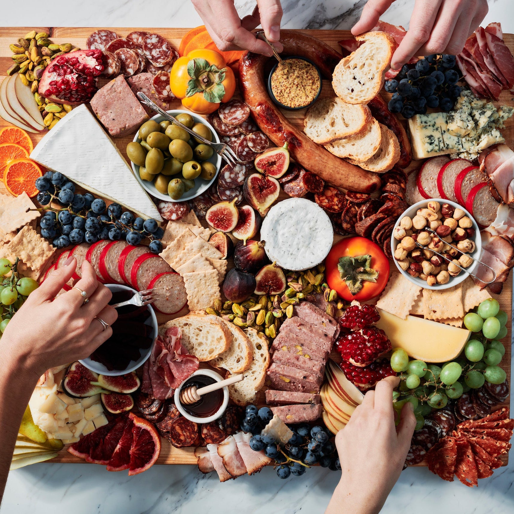 Charcuterie board with various meats, cheeses, fruits, and vegetables on a marble surface.
