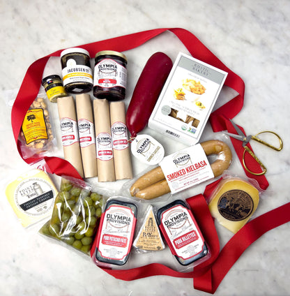 Assorted food items including sausages, olives, and jars on a white surface with red ribbons.