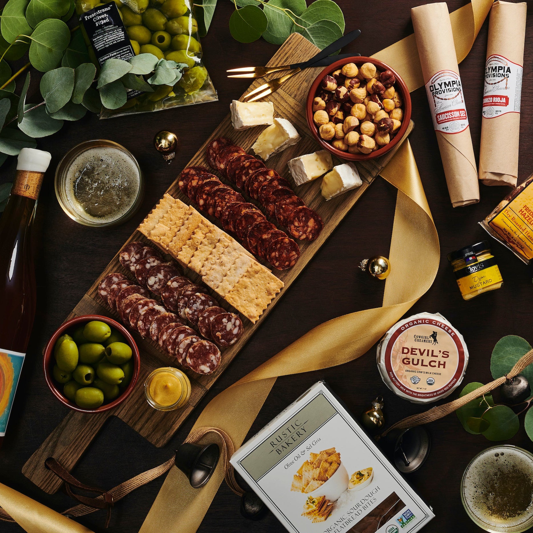 Gourmet platter with assorted foods, including meats, cheeses, and olives, on a dark surface with greenery.