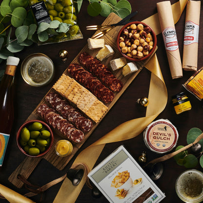 Gourmet platter with assorted foods, including meats, cheeses, and olives, on a dark surface with greenery.